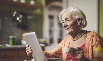 Seniorin, die in ihrer Küche auf einen Tablet-Computer schaut