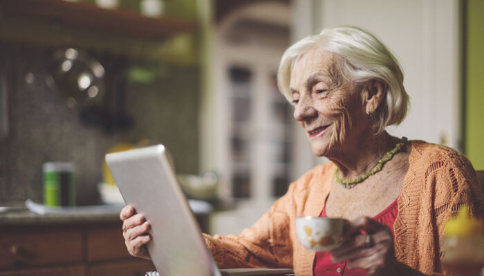 Seniorin, die in ihrer Küche auf einen Tablet-Computer schaut