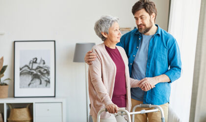 Eine ältere Frau, die eine Gehhilfe benutzt und mit ihrem Betreuer spricht, der ihr bei der Rehabilitation hilft