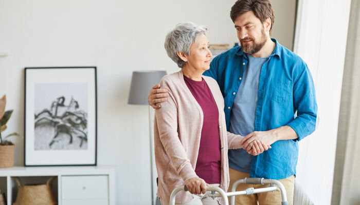 Eine ältere Frau, die eine Gehhilfe benutzt und mit ihrem Betreuer spricht, der ihr bei der Rehabilitation hilft