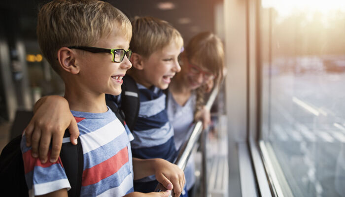 Kinder im Alter von 7 und 11 Jahren beobachten Flugzeuge durch die Fenster der Lobby und haben Spaß