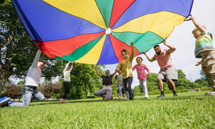 Kinder spielen mit einem bunten Fallschirm und ein Junge rennt darunter hindurch.