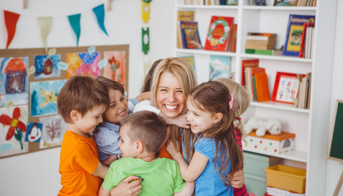 Kinder im Kindergarten umarmen ihre Erzieherin.