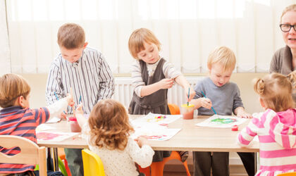 Kinder und Erzieherin malen im Kindergarten mit Pinsel und Wasserfarben auf Papier