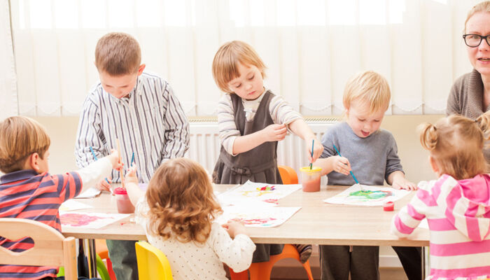 Kinder und Erzieherin malen im Kindergarten mit Pinsel und Wasserfarben auf Papier