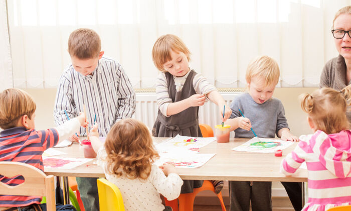 Kinder und Erzieherin malen im Kindergarten mit Pinsel und Wasserfarben auf Papier