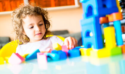 Kleines Mädchen, das im Kindergarten ein Haus aus Bauklötzen baut.