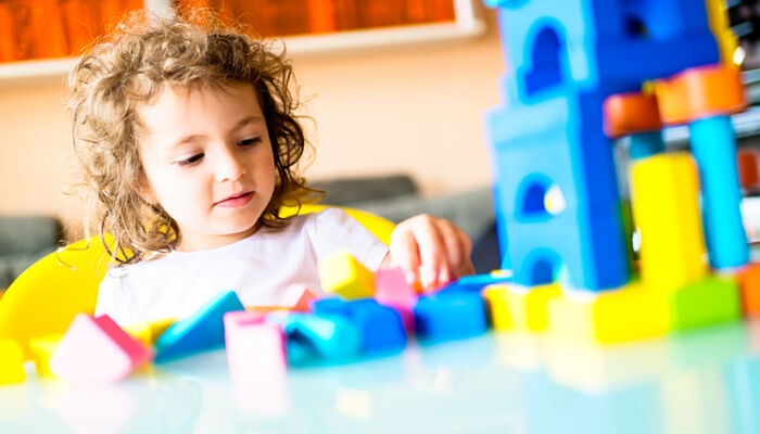 Kleines Mädchen, das im Kindergarten ein Haus aus Bauklötzen baut.