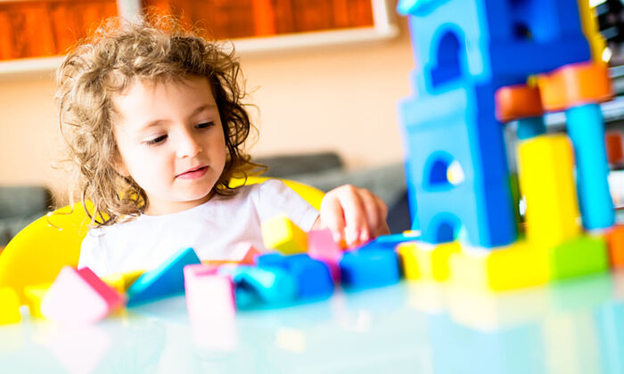 Kleines Mädchen, das im Kindergarten ein Haus aus Bauklötzen baut.