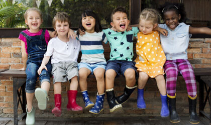 Kindergarten-Kinder sitzen lachend Arm in Arm auf einer Bank