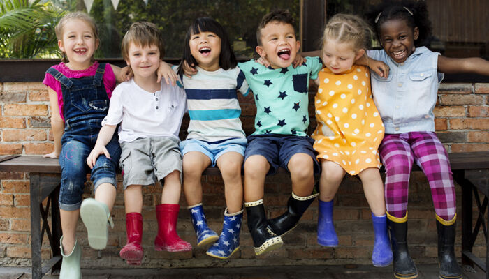 Kindergarten-Kinder sitzen lachend Arm in Arm auf einer Bank