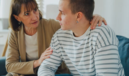 Eine Mutter tröstet ihren Sohn im Teenageralter in einem schwierigen emotionalen Moment auf dem Sofa im Wohnzimmer zu Hause