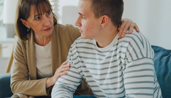 Eine Mutter tröstet ihren Sohn im Teenageralter in einem schwierigen emotionalen Moment auf dem Sofa im Wohnzimmer zu Hause