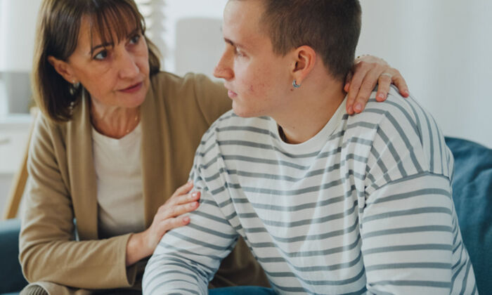 Eine Mutter tröstet ihren Sohn im Teenageralter in einem schwierigen emotionalen Moment auf dem Sofa im Wohnzimmer zu Hause
