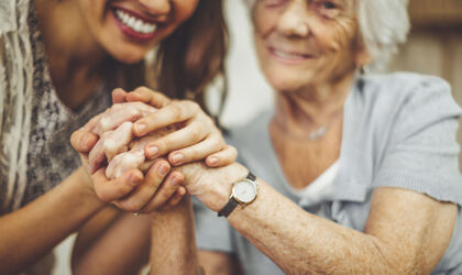 Nahaufnahme einer lächelnden Pflegekraft, die die Hand einer älteren Frau hält.
