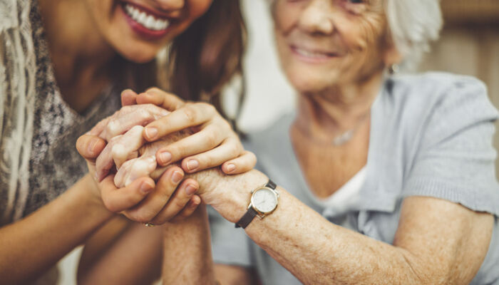Nahaufnahme einer lächelnden Pflegekraft, die die Hand einer älteren Frau hält.