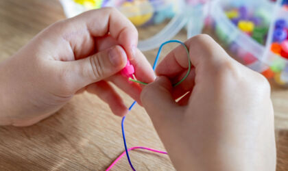 Kinderhände fädeln bunte Perlen auf eine Schnur