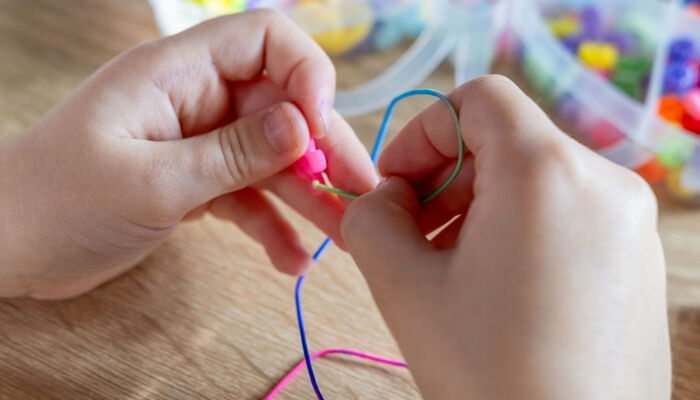 Kinderhände fädeln bunte Perlen auf eine Schnur