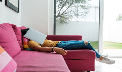 Eine Person liegt resigniert auf dem Sofa, den aufgeklappte Laptop vorm Gesicht