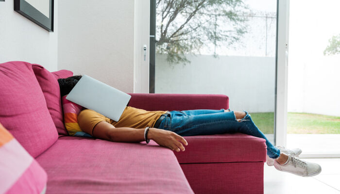 Eine Person liegt resigniert auf dem Sofa, den aufgeklappte Laptop vorm Gesicht
