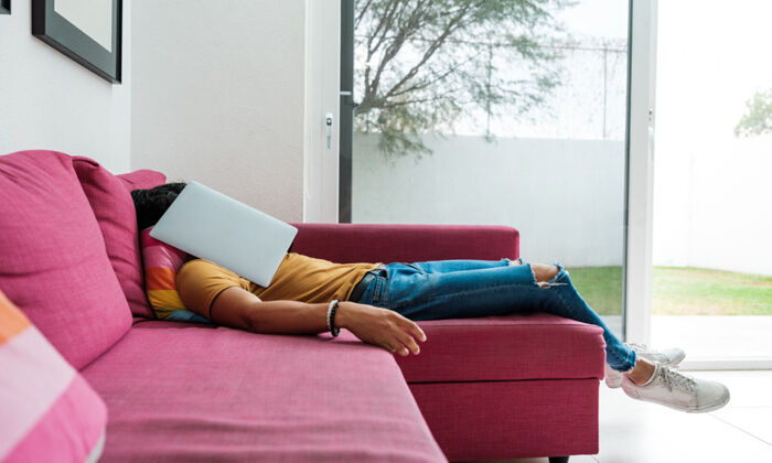 Eine Person liegt resigniert auf dem Sofa, den aufgeklappte Laptop vorm Gesicht