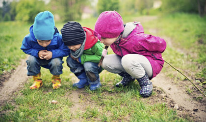 Drei Kinder im Alter von 5 und 8 Jahren schauen auf eine Schnecke im Gras