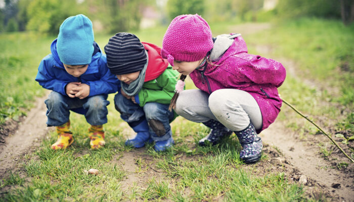 Drei Kinder im Alter von 5 und 8 Jahren schauen auf eine Schnecke im Gras