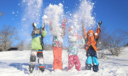 Vier Kinder spielen im Winter im Schnee und wirbeln ihn in die Luft