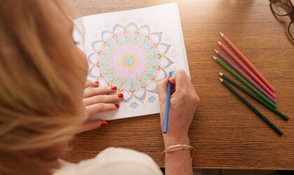 Eine erwachsene Frau mal mit farbigen Buntstiften ein Mandala aus.