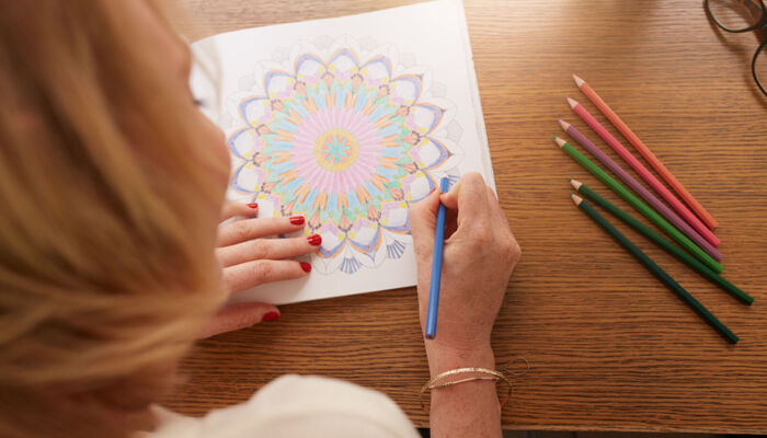 Eine erwachsene Frau mal mit farbigen Buntstiften ein Mandala aus.