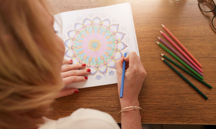Eine erwachsene Frau mal mit farbigen Buntstiften ein Mandala aus.