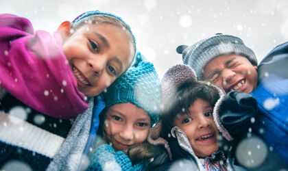 Vier Kinder in Winterkleidung schauen in die Kamera und freuen sich über den Schnee