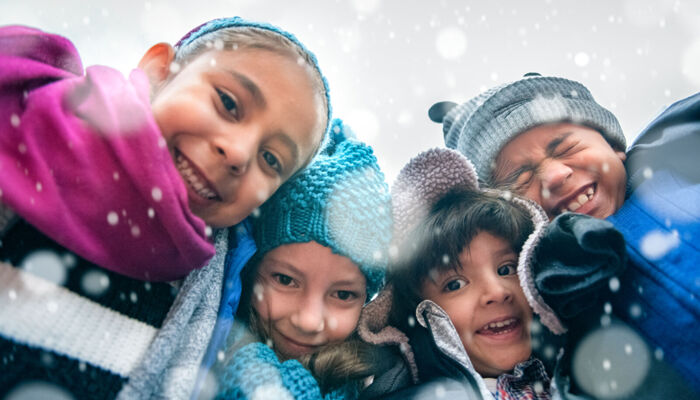 Vier Kinder in Winterkleidung schauen in die Kamera und freuen sich über den Schnee