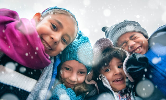 Vier Kinder in Winterkleidung schauen in die Kamera und freuen sich über den Schnee