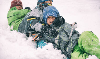 Three children in colorful snowsuits are playing in the snow