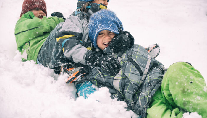 Drei Kinder in bunten Schneeanzügen toben im Schnee