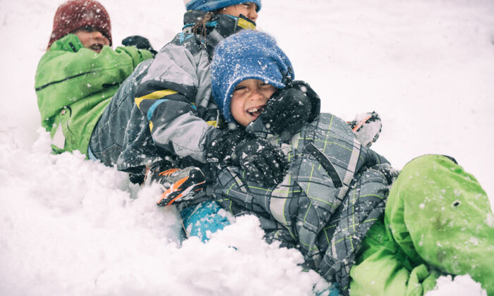 Drei Kinder in bunten Schneeanzügen toben im Schnee