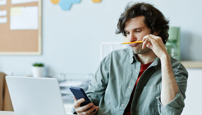 Gelangweilter junger Mann im Büro mit Smartphone