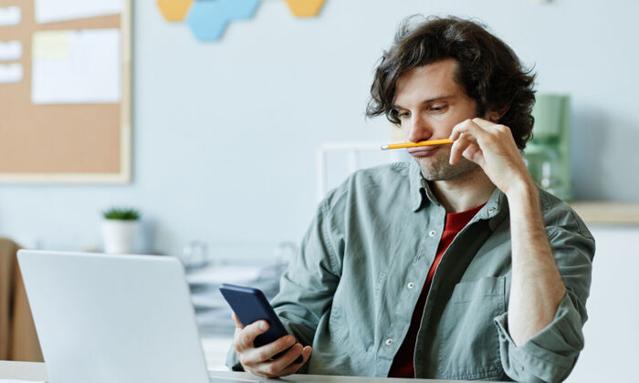 Gelangweilter junger Mann im Büro mit Smartphone