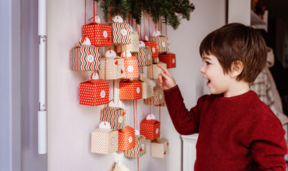 ein kleiner Junge zeigt auf einen handgemachten Adventskalender an der Wand