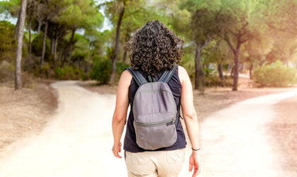 Frau mit Rucksack, die im Wald vor einer Weggabelung steht