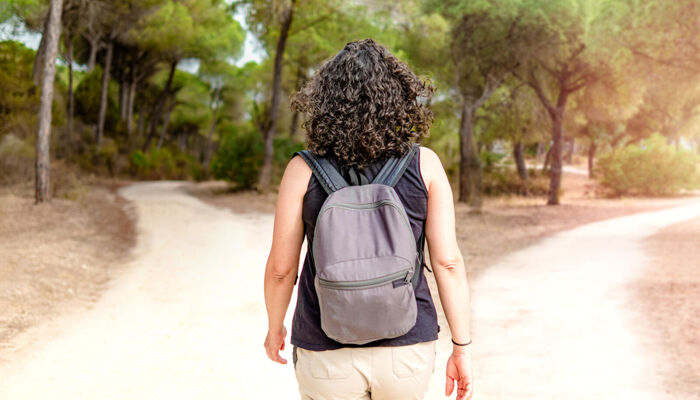 Frau mit Rucksack, die im Wald vor einer Weggabelung steht