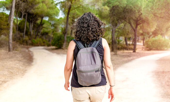 Frau mit Rucksack, die im Wald vor einer Weggabelung steht