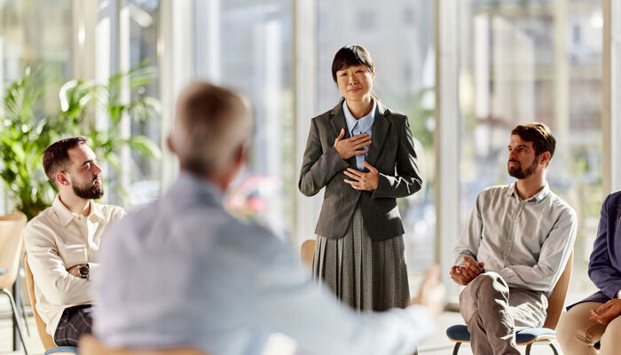 Belastete weibliche asiatische Business Unternehmerin spricht in Gruppen Therapie Sitzung im Büro.