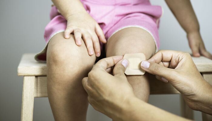 Mutter legt ein Pflaster auf das Knie ihrer Tochter