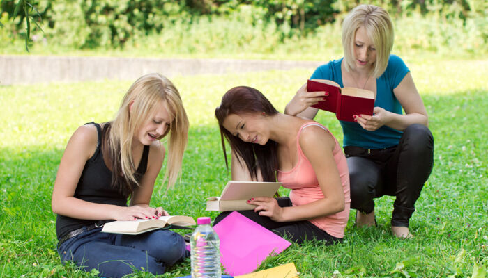 drei Teenagerinnen lesen Bücher auf einer grünen Weise unter einem Baum im Schatten