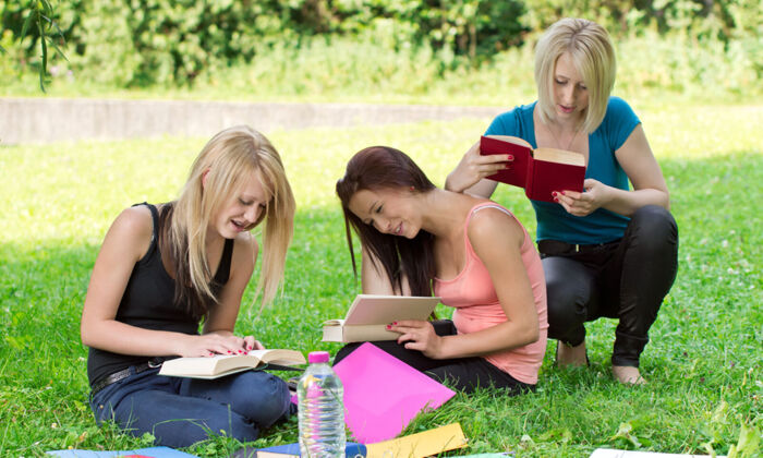 drei Teenagerinnen lesen Bücher auf einer grünen Weise unter einem Baum im Schatten