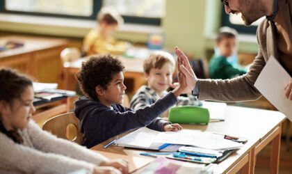 lachender Lehrer gibt einem Grundschüler im Klassenzimmer High-Five