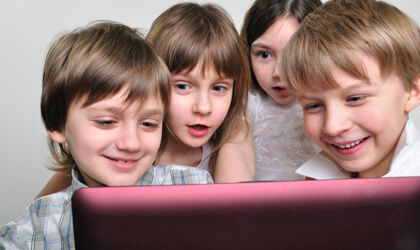 eine Gruppe von 7-8 jährigen schaut freudig auf den Bildschirm eines Tabletcomputers