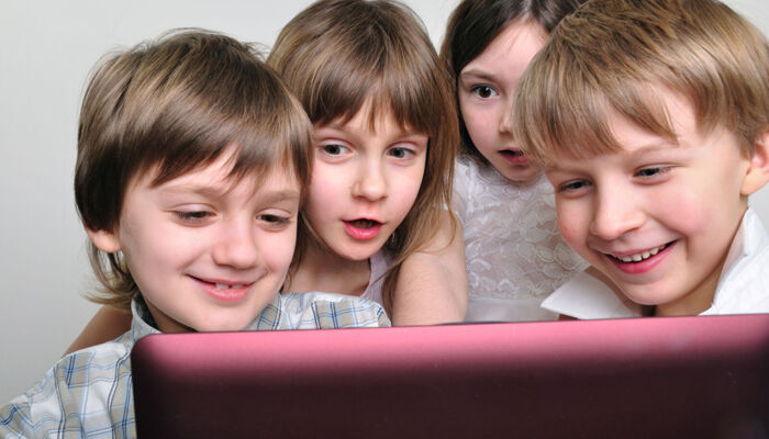 eine Gruppe von 7-8 jährigen schaut freudig auf den Bildschirm eines Tabletcomputers